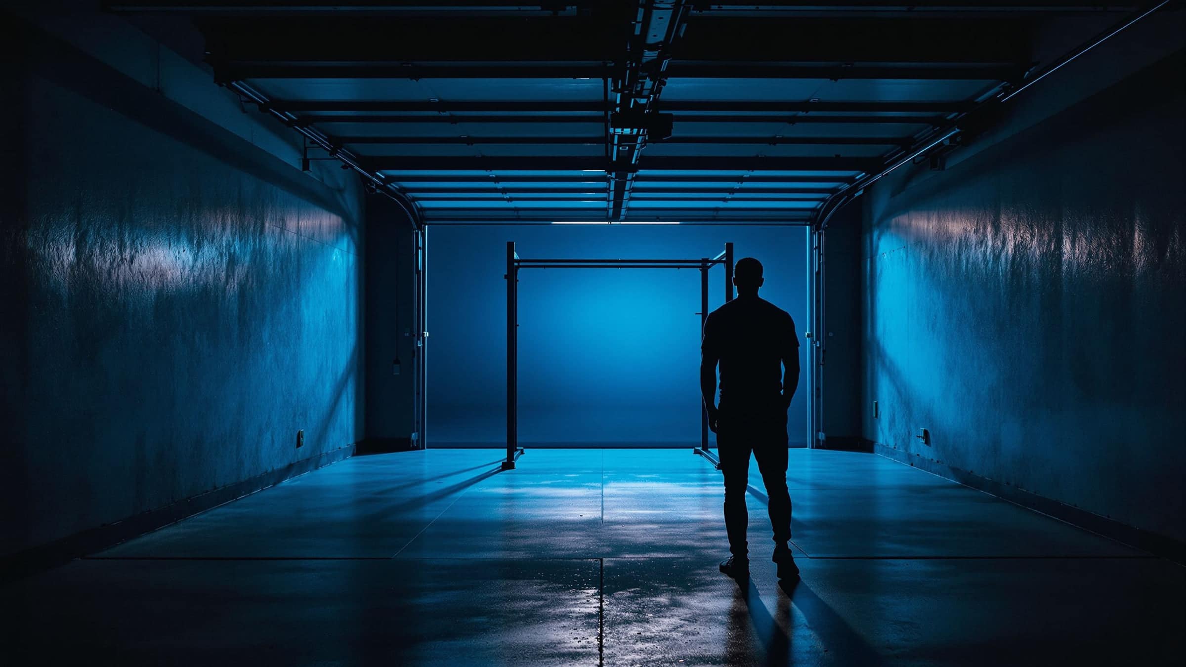 An empty garage gym with a power rack in blue light.